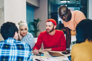 Diverse team of young people dressed in smart casual wear communicating with each other and discussing ideas for design project having brainstorming meeting.Collaborative process of creative students
